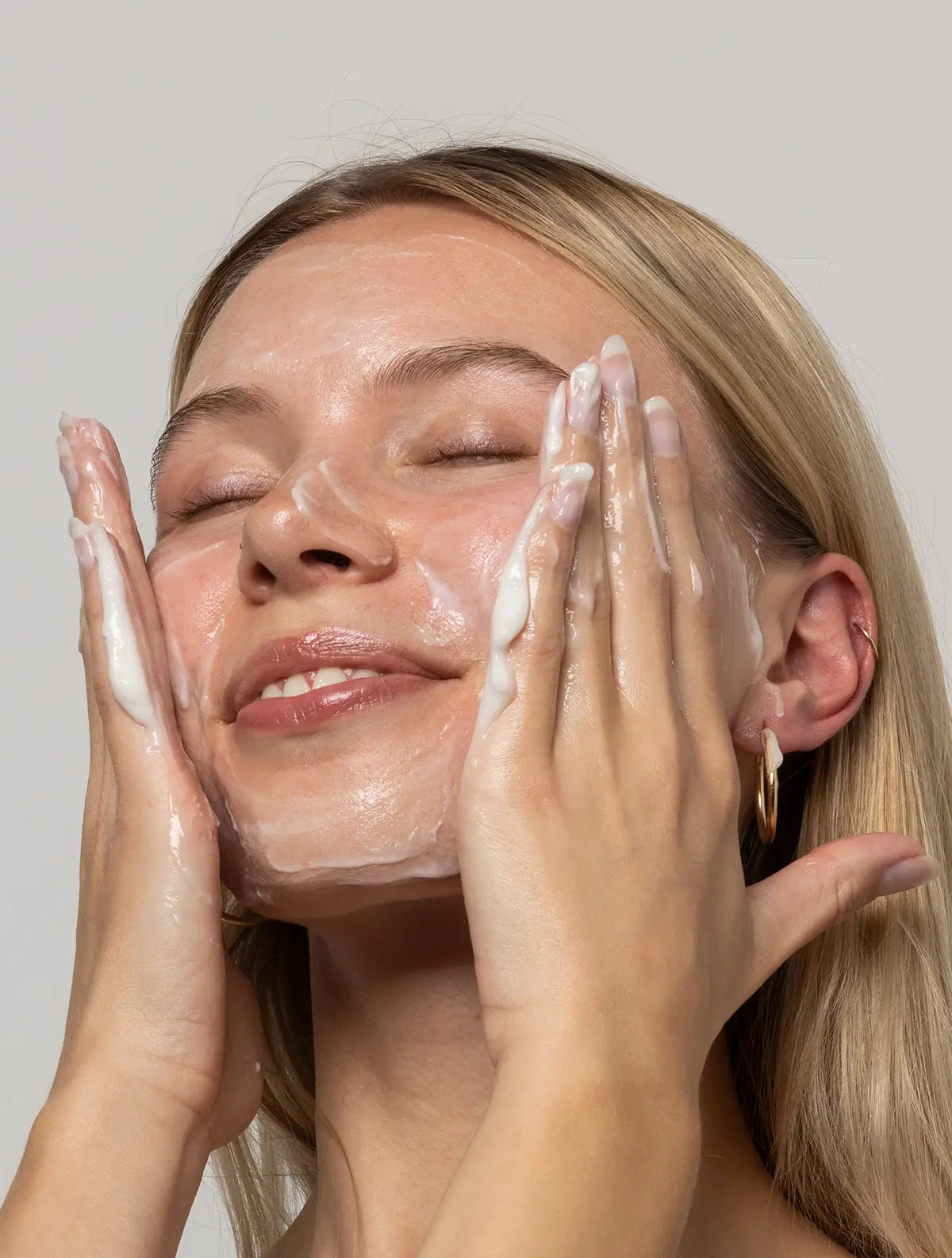 Model smiling washing her face with OhWhippy cleanser